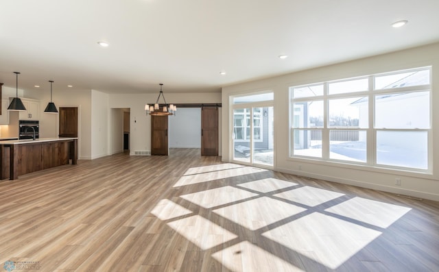 unfurnished living room featuring light wood-style flooring, baseboards, a barn door, and recessed lighting