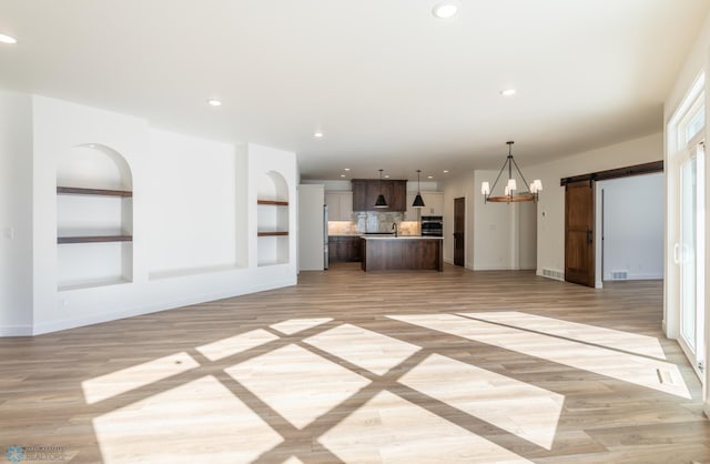 unfurnished living room with a barn door, light wood-type flooring, baseboards, recessed lighting, and built in features