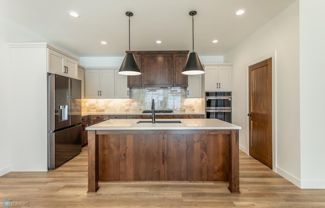 kitchen featuring appliances with stainless steel finishes, light countertops, a kitchen island with sink, a sink, and recessed lighting