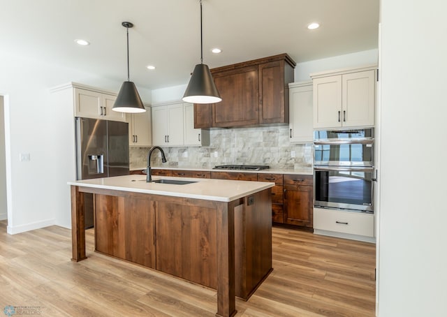 kitchen with a sink, light wood-type flooring, appliances with stainless steel finishes, light countertops, and decorative backsplash