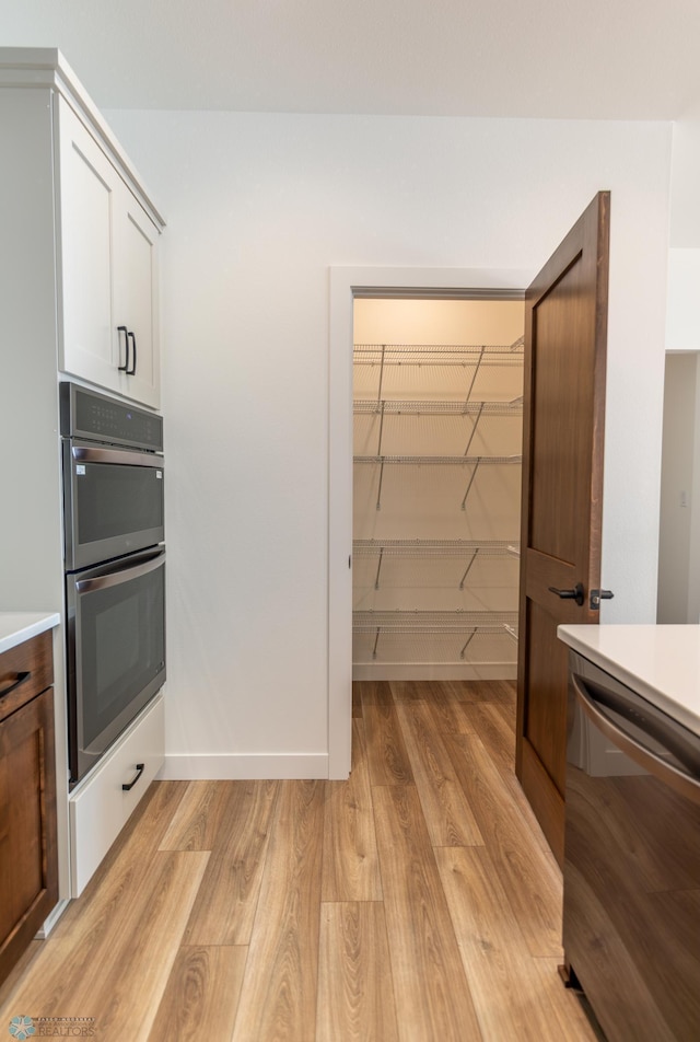 kitchen with appliances with stainless steel finishes, light wood-type flooring, light countertops, and baseboards