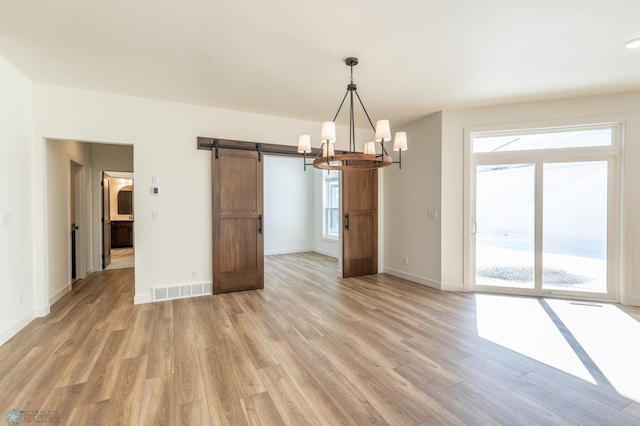 unfurnished dining area featuring light wood-type flooring, a barn door, a chandelier, and baseboards