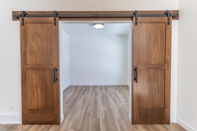 spare room featuring a barn door, light wood-style floors, and baseboards