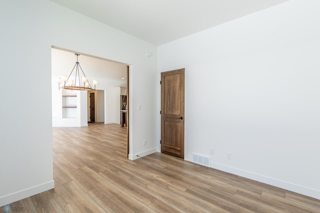 spare room featuring a chandelier, light wood-style floors, and baseboards