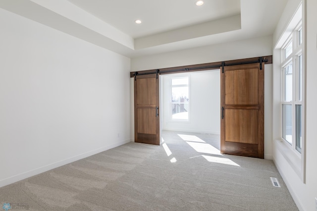 unfurnished room featuring a barn door, light colored carpet, plenty of natural light, and recessed lighting