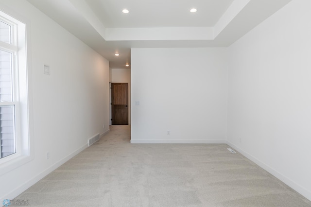 empty room featuring light colored carpet, a tray ceiling, recessed lighting, and baseboards