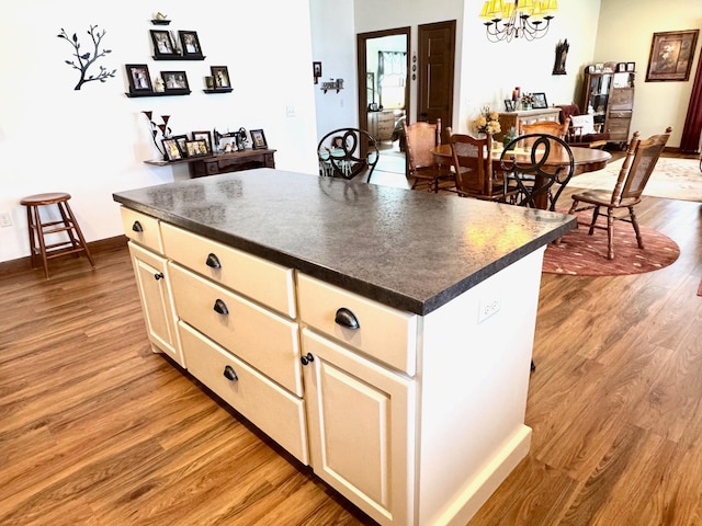 kitchen featuring light wood-style flooring, a notable chandelier, baseboards, a center island, and dark countertops