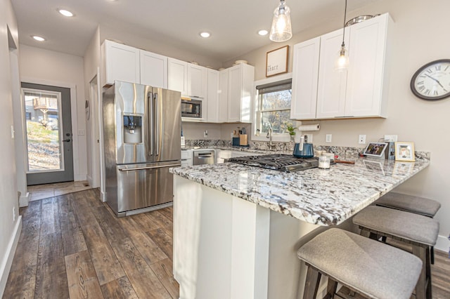 kitchen with stainless steel appliances, a peninsula, white cabinetry, a kitchen breakfast bar, and hanging light fixtures