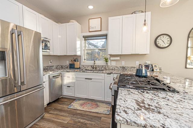 kitchen with decorative light fixtures, dark wood finished floors, appliances with stainless steel finishes, white cabinets, and a sink