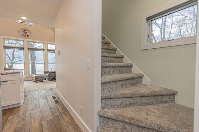 stairway with lofted ceiling, hardwood / wood-style flooring, a water view, visible vents, and baseboards