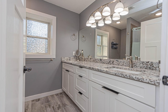 bathroom featuring double vanity, baseboards, wood finished floors, a shower stall, and a sink