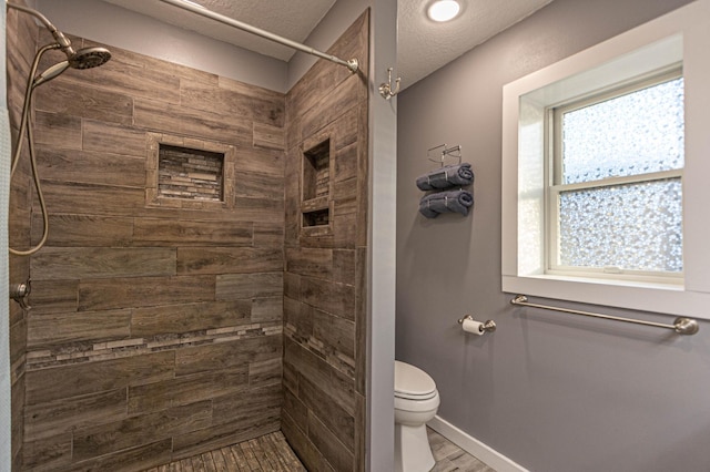 bathroom featuring wood finished floors, a tile shower, toilet, and baseboards