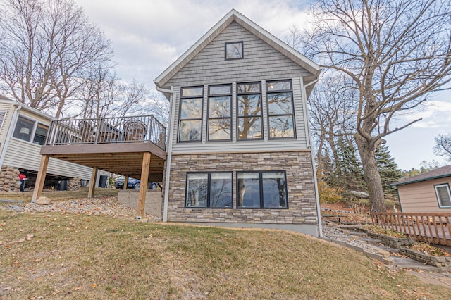 rear view of house with a yard, stone siding, a wooden deck, and a sunroom