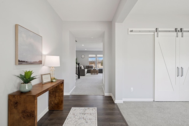 corridor featuring dark wood-type flooring, a barn door, baseboards, and dark carpet