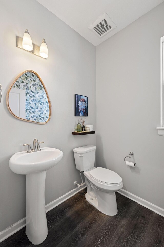 half bath with visible vents, toilet, baseboards, and wood finished floors