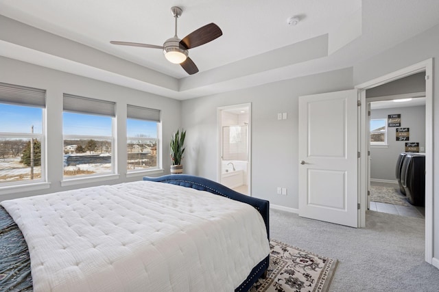 bedroom featuring light colored carpet, baseboards, ensuite bathroom, and a tray ceiling