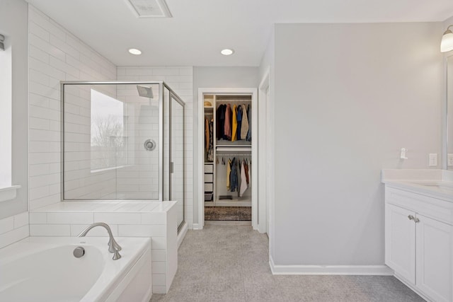 bathroom with vanity, baseboards, a stall shower, a walk in closet, and a garden tub