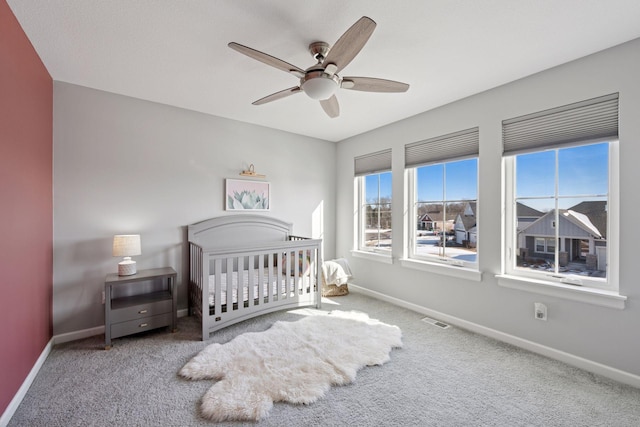 bedroom featuring a crib, carpet flooring, baseboards, and visible vents