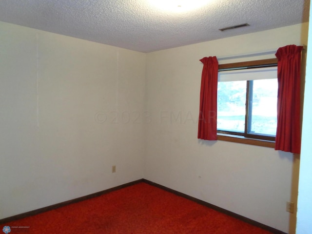 spare room featuring carpet floors, baseboards, visible vents, and a textured ceiling