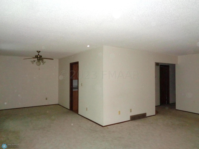 spare room featuring a textured ceiling, light colored carpet, visible vents, baseboards, and a ceiling fan