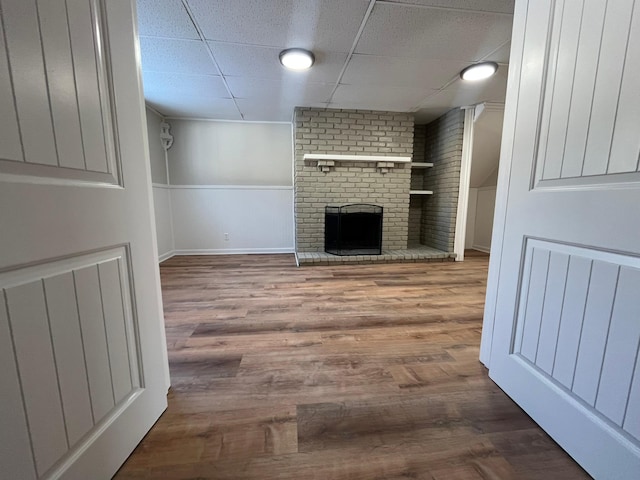 unfurnished living room featuring a paneled ceiling, a brick fireplace, and wood finished floors