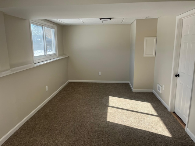 carpeted spare room featuring a drop ceiling and baseboards