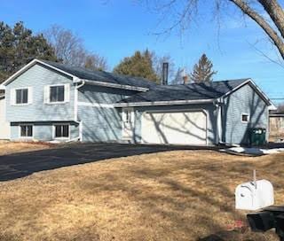 view of side of home featuring a garage, aphalt driveway, and a lawn