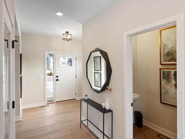 foyer entrance featuring baseboards, a textured ceiling, and light wood finished floors