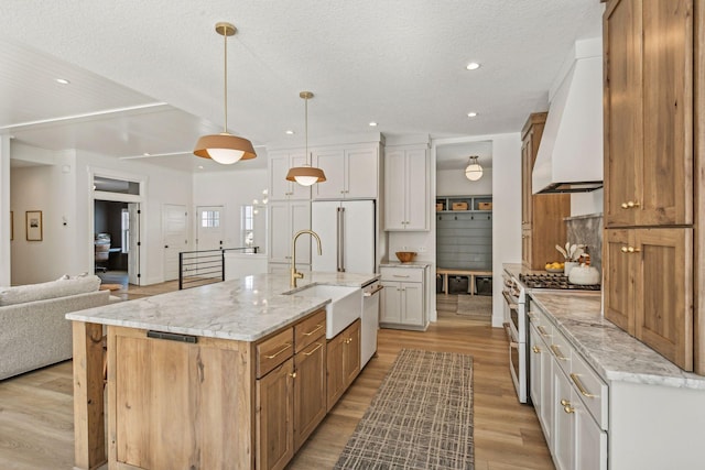 kitchen featuring wall chimney range hood, a spacious island, white cabinetry, and high end appliances