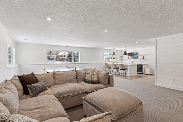 living room with light carpet, wine cooler, a textured ceiling, and bar area