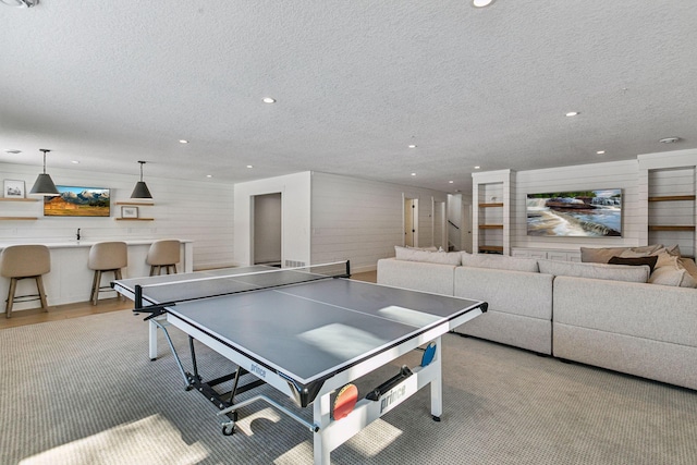 game room featuring light wood-style floors, recessed lighting, bar area, and a textured ceiling