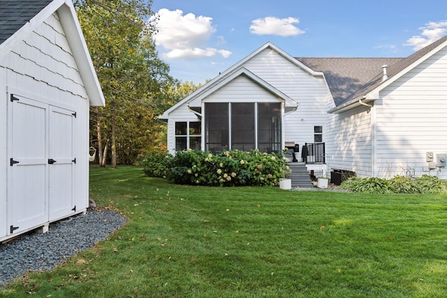 back of property with an outbuilding, a storage shed, a sunroom, a yard, and roof with shingles