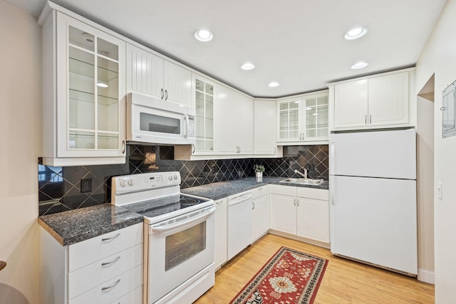kitchen with dark countertops, glass insert cabinets, a sink, light wood-type flooring, and white appliances