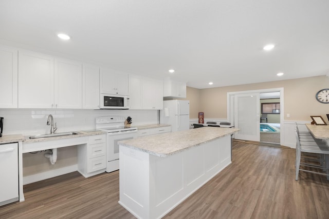 kitchen with white appliances, wood finished floors, a kitchen island, white cabinets, and light countertops