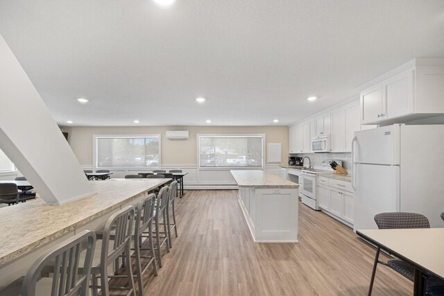 kitchen with white appliances, white cabinets, an AC wall unit, light wood-type flooring, and a center island