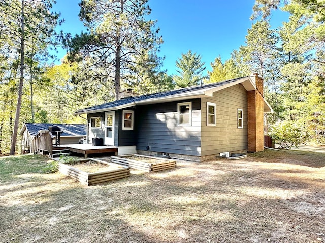 back of property with a chimney, a wooden deck, and a garden