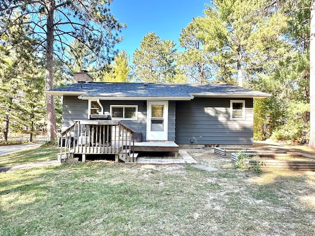 view of front of home with a front yard, roof with shingles, a chimney, and a wooden deck