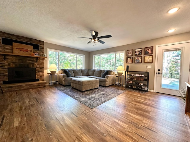 living area with a textured ceiling, a fireplace, wood finished floors, a ceiling fan, and baseboards