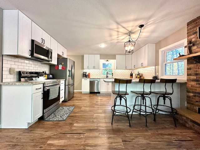 kitchen with white cabinets, dark wood-style floors, a kitchen breakfast bar, stainless steel appliances, and pendant lighting