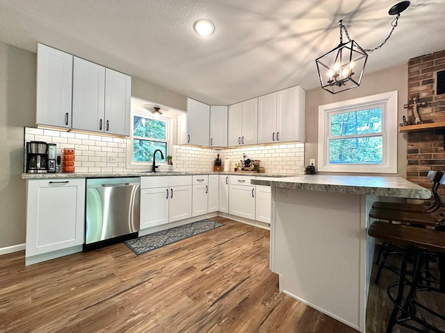 kitchen featuring dishwasher, a kitchen bar, white cabinetry, pendant lighting, and a sink