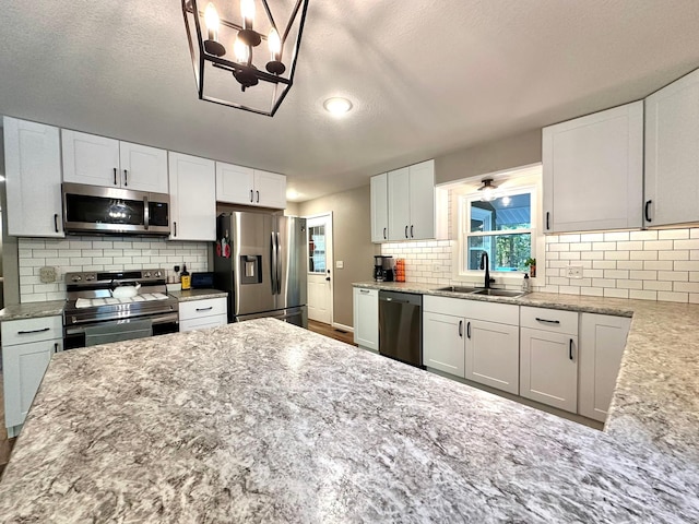 kitchen with stainless steel appliances, a sink, white cabinets, light stone countertops, and tasteful backsplash