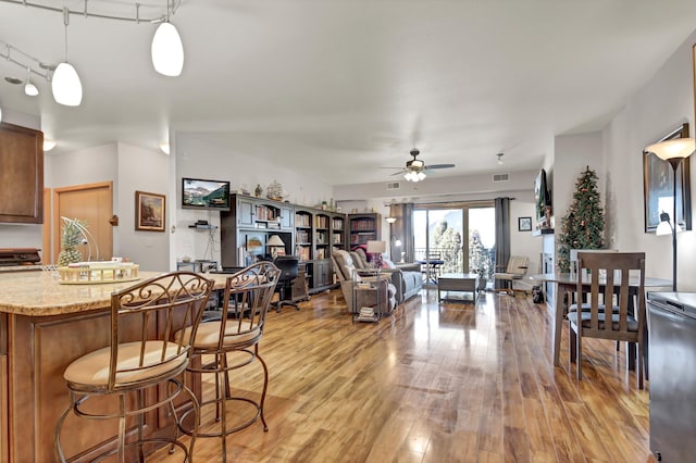 kitchen featuring light wood finished floors, brown cabinetry, open floor plan, decorative light fixtures, and light stone countertops