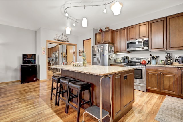 kitchen with light wood-style flooring, a kitchen island, appliances with stainless steel finishes, and pendant lighting