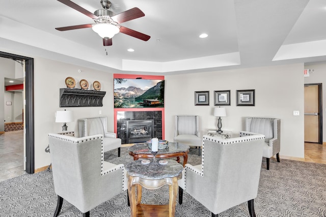 living room with recessed lighting, a ceiling fan, baseboards, a tray ceiling, and a tiled fireplace