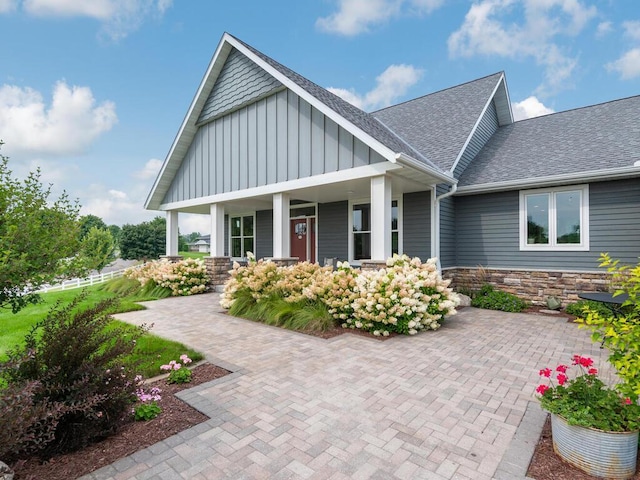 view of front of house featuring stone siding, a shingled roof, board and batten siding, and a porch