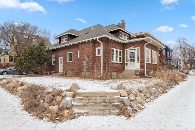 view of snowy exterior featuring entry steps, a chimney, and brick siding