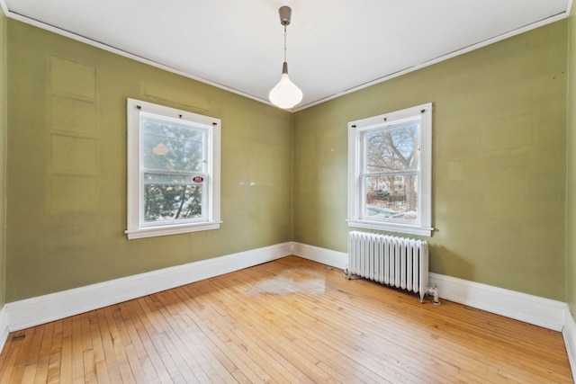 spare room featuring ornamental molding, baseboards, radiator heating unit, and wood finished floors