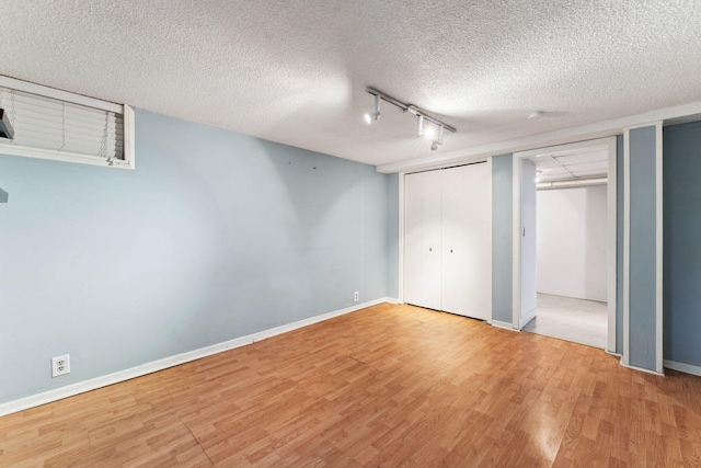 unfurnished bedroom featuring a textured ceiling, wood finished floors, multiple closets, baseboards, and track lighting