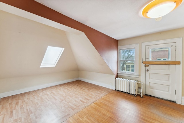 bonus room featuring baseboards, lofted ceiling with skylight, light wood-type flooring, and radiator