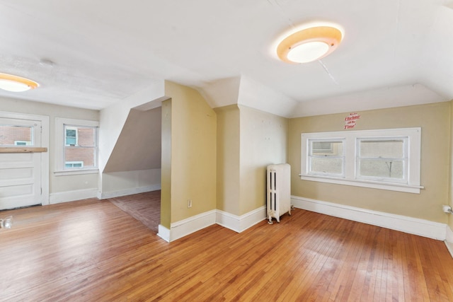 additional living space featuring light wood-type flooring, lofted ceiling, baseboards, and radiator heating unit